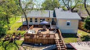 Une maison à deux étages avec une terrasse, un petit pont et un étang.