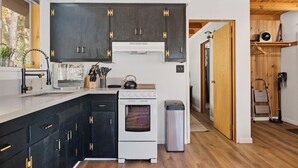 A modern kitchen with dark cabinets, a white stove, and a trash bin.