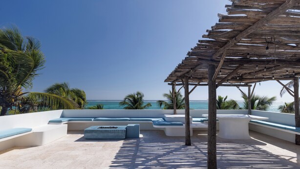 Zona relax in spiaggia con sedute integrate e un pergolato in legno.