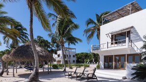 Una proprietà fronte spiaggia con un edificio bianco, palme e una struttura con tetto di paglia.