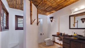 Un bagno con soffitto in bambù, un WC, un lavabo con specchio e un porta asciugamani.