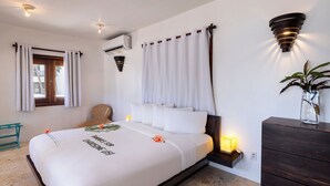 Camera d'albergo con un letto, un comodino, una cassettiera, una finestra con tende e illuminazione a parete.