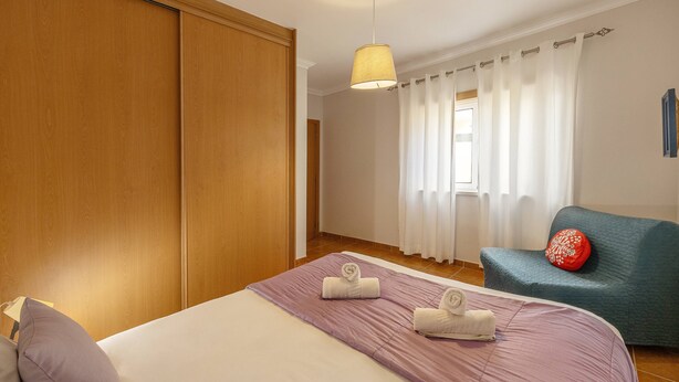 Una habitación de hotel con cama, una silla, armario y ventana con cortinas.