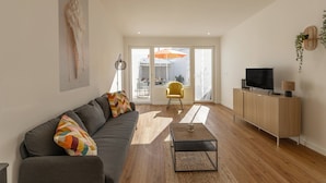 Un soggiorno moderno con un divano grigio, una poltrona gialla, un mobile in legno con un televisore e un'ampia finestra con un ombrello all'esterno.