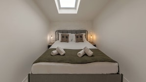 Una camera da letto con un lucernario, un letto con cuscini, una coperta verde e lampade da comodino.