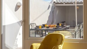 Una poltrona gialla a dondolo in una stanza con ampie finestre che si affacciano su un balcone con tavolo e ombrellone arancione.