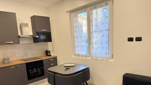 Cocina compacta con electrodomésticos modernos, comedor con mesa y sillas, y ventana con cortinas florales.