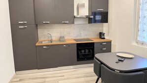 Una cocina compacta con armarios oscuros, un lavamanos de acero inoxidable, un microondas y un horno empotrado.