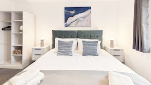 Une chambre à coucher bien rangée, avec un grand lit, des tables de chevet, une armoire et un tableau accroché au mur.