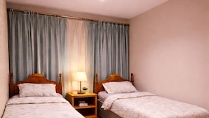 Une chambre avec deux lits simples, un plancher en bois, une table de chevet avec une lampe et un luminaire au plafond.