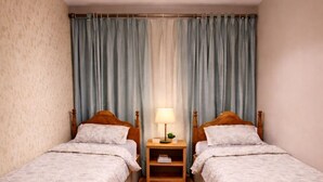 Une chambre avec deux lits simples, des têtes de lit en bois, une table de chevet avec une lampe et un plancher en bois.