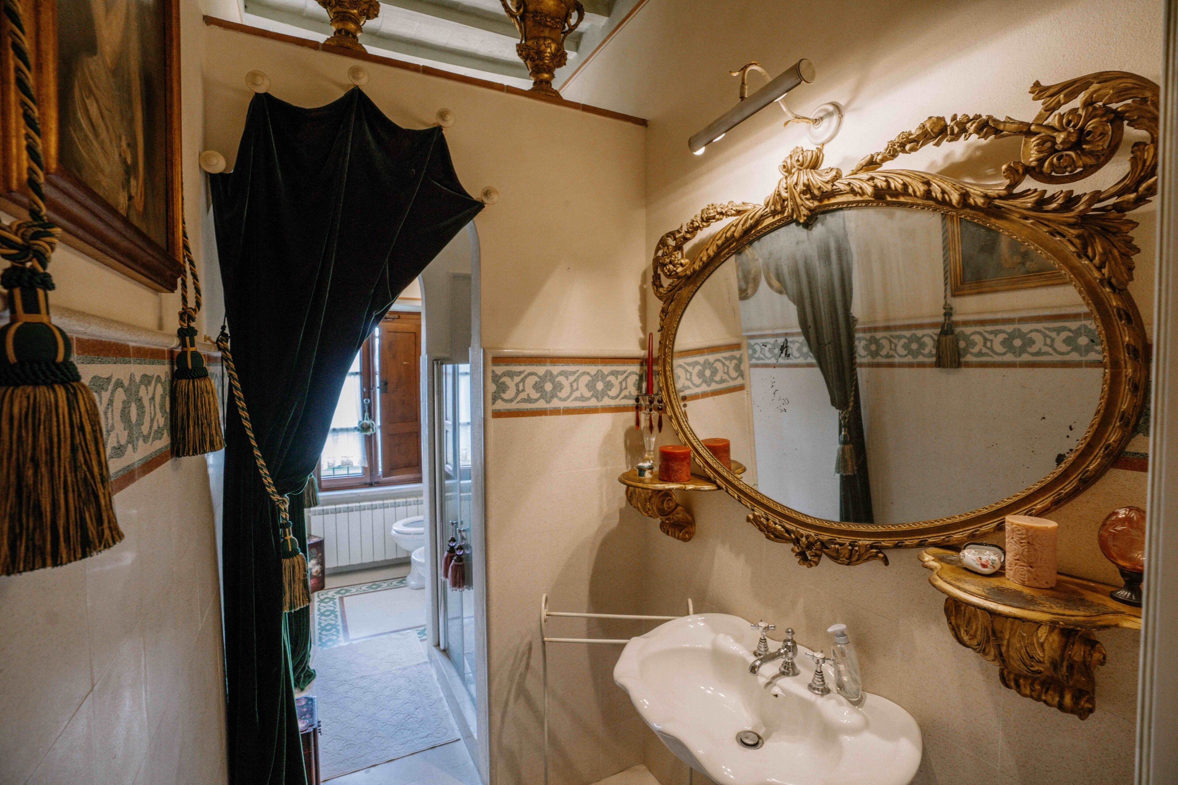 A bathroom with a large ornate mirror, a white sink, and a shower area.
