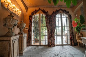 Ein Zimmer mit einem großen Bogenfenster, verzierten Vorhängen und einer Wandleuchte.