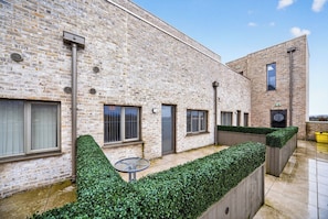 A courtyard with a brick building, a small table, and neatly trimmed hedges. - Amber Vista Apartments Cardiff (Cardiff)