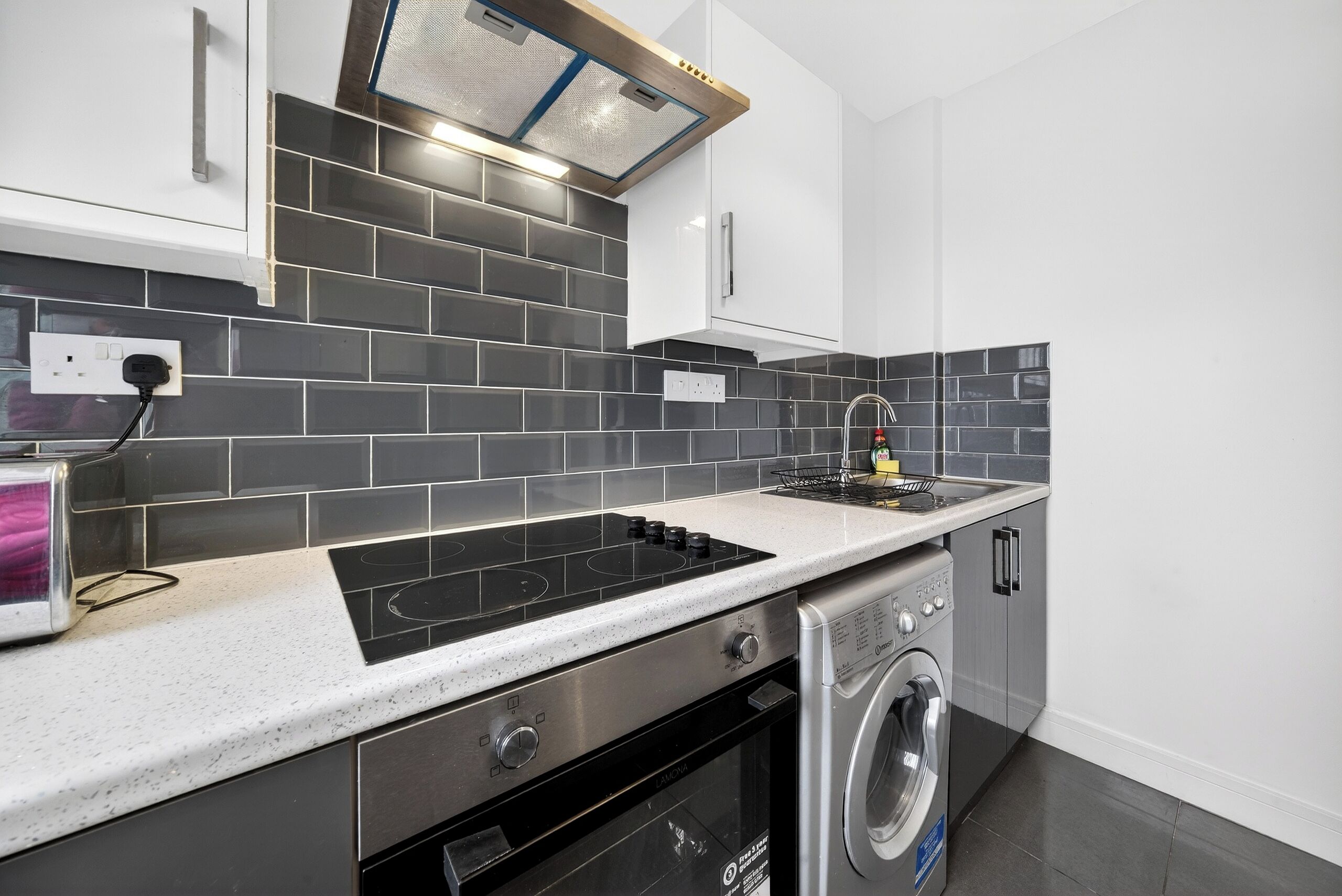 A modern kitchen with a built-in stove, a washing machine, and a tiled backsplash.