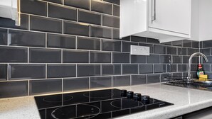 A kitchen with black tiled backsplash, a stainless steel range hood, and a gas stove. - Amber Vista Apartments Cardiff (Cardiff)