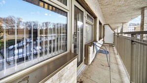A balcony with a view of parked cars and trees, a metal chair, and a stone wall. - Amber Vista Apartments Cardiff (Cardiff)
