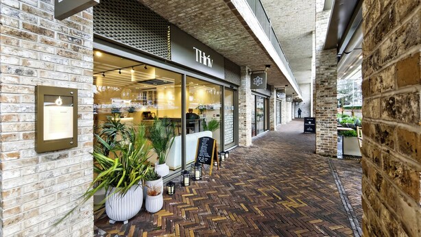 A corridor with a brick wall on one side and a storefront with a sign reading "BODE EGA" and "THIN". - Amber Vista Apartments Cardiff (Cardiff)