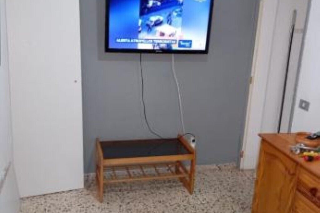 A room with a television mounted on the wall, a wooden bench, and a wooden dresser.