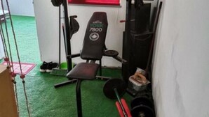 Une salle de sport équipée d’un banc portant l’inscription « YORK 7800 », de disques de poids et d’une barre d’haltères.