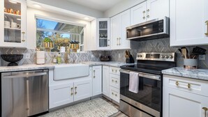 Une cuisine moderne avec des meubles blancs, des appareils en acier inoxydable et un dosseret de carrelage disposé en motif chevron.