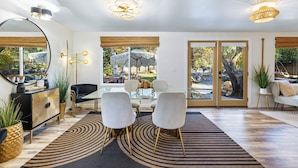 Un salon moderne avec une console noire et dorée, des chaises blanches et une grande fenêtre donnant sur l’extérieur.