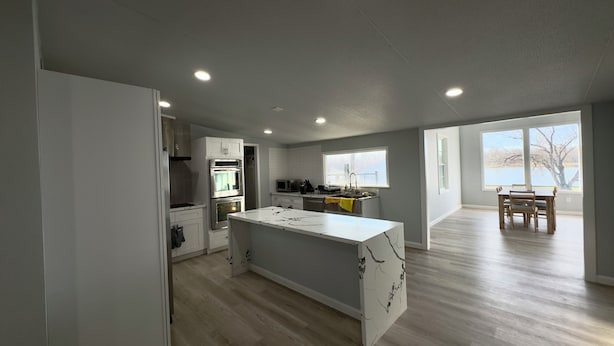 Una cocina moderna con armarios blancos, una isla central y un comedor con vista a un lago.