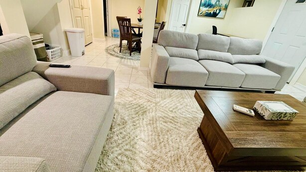 Una sala de estar con un sofá color beige, un sofá seccional gris, una mesa de centro de madera y una alfombra mullida blanca.