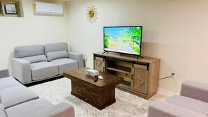 Una sala de estar con un sofá gris, una mesa de centro de madera y un televisor sobre un mueble de madera.