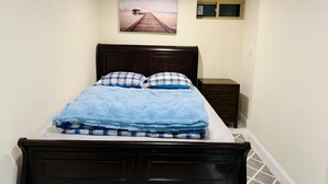 Un dormitorio con cama, mesita de noche, ventana y un cuadro en la pared.
