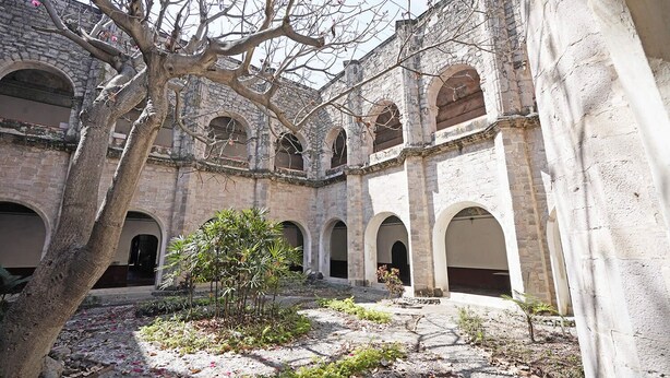 Um edifício antigo de pedra com portas arqueadas e um pátio com uma árvore e plantas.