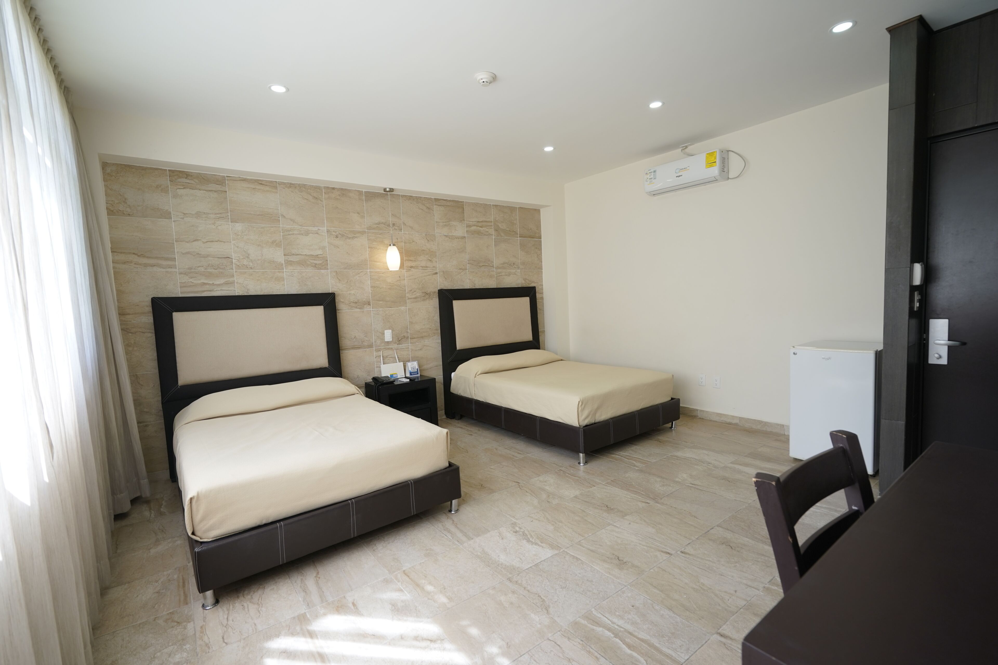 Habitación de hotel con dos camas, un escritorio, una silla y un refrigerador.