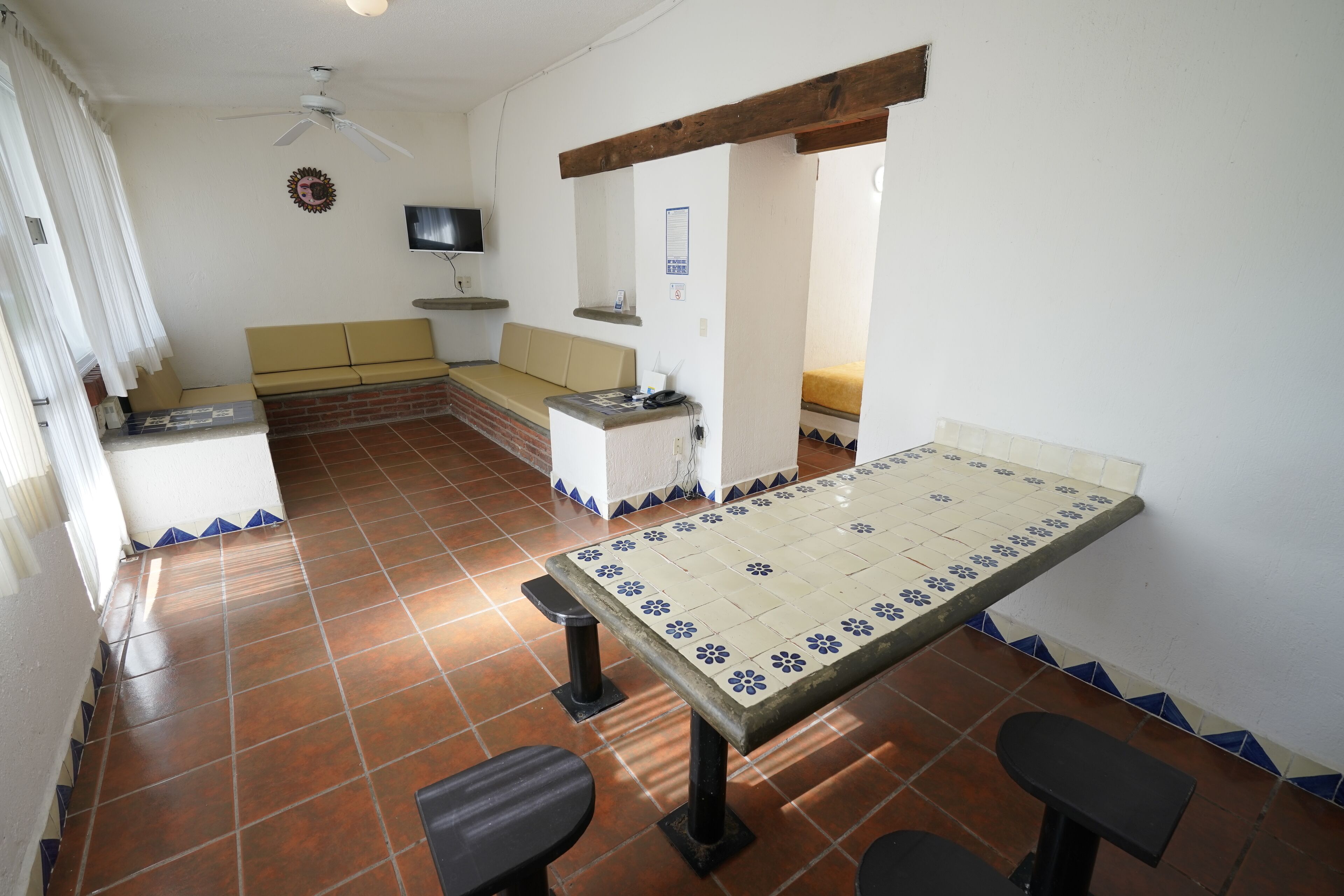A room with a tiled floor, a table with chairs, a sofa, a television, and a ceiling fan.