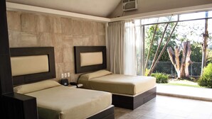Quarto de hotel com duas camas, uma janela grande e vista para o verde.