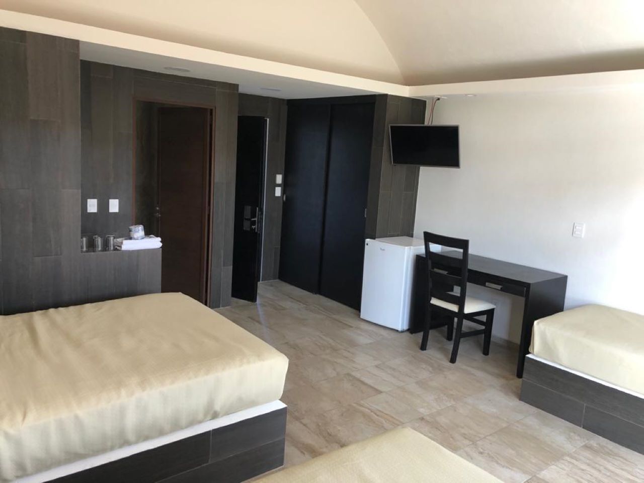 Une chambre d’hôtel avec deux lits, un bureau, une chaise, une télévision et une petite kitchenette.