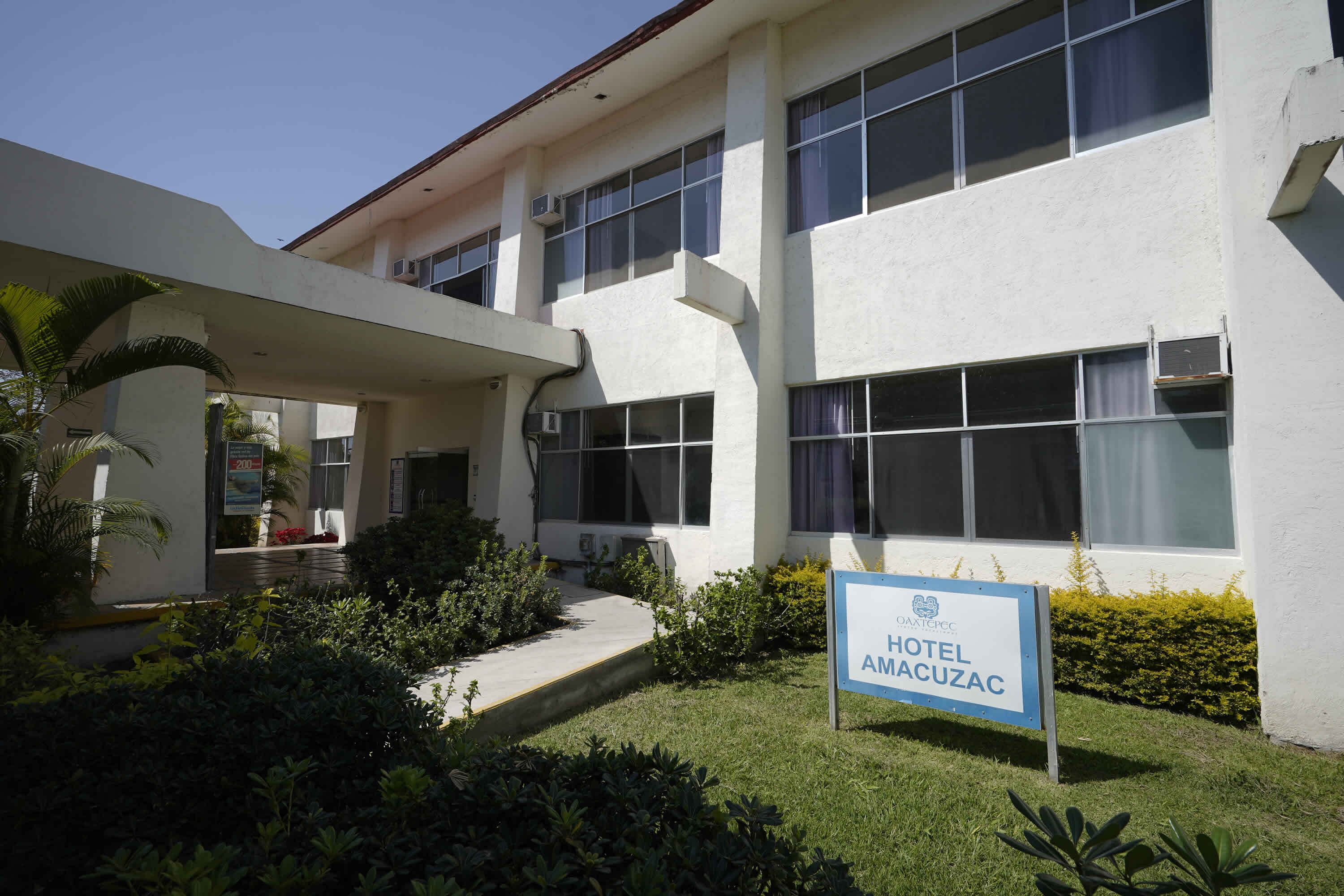 A hotel with a sign reading 'HOTEL AMACUZAC,' a covered entrance, and a well-maintained lawn.