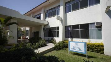 A hotel with a sign reading 'HOTEL AMACUZAC,' a covered entrance, and a well-maintained lawn.