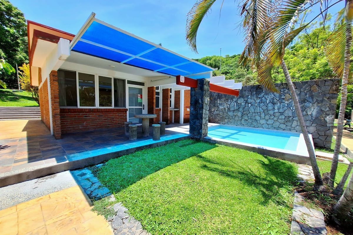 A modern house with a swimming pool, a covered patio, and a stone wall.