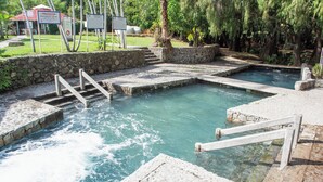 Uma piscina de pedra com degraus que a levam, rodeada por um muro de pedra e vegetação.
