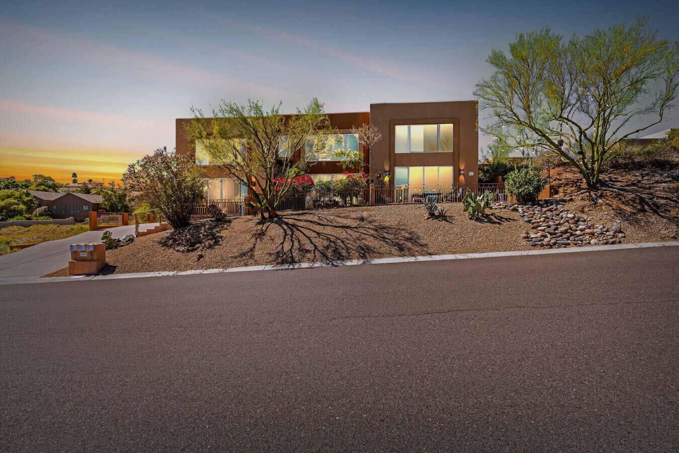 A modern two-story building with a flat roof, large windows, and a landscaped garden with desert plants.