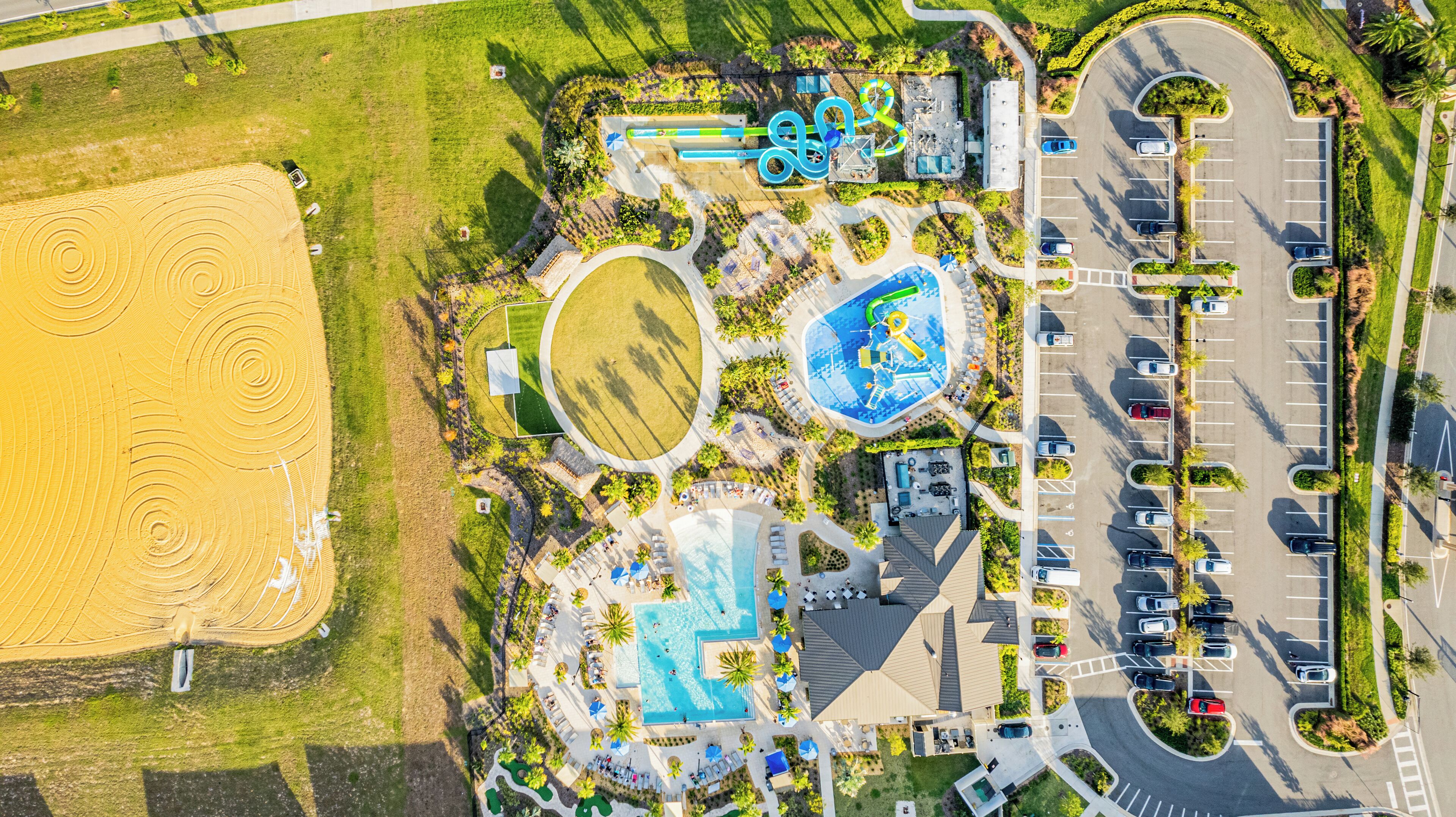 Vista aérea de um resort com uma extensa área arenosa, piscina e estacionamento.
