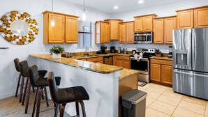 A modern kitchen with wooden cabinets, stainless steel appliances, a granite countertop, and bar stools.