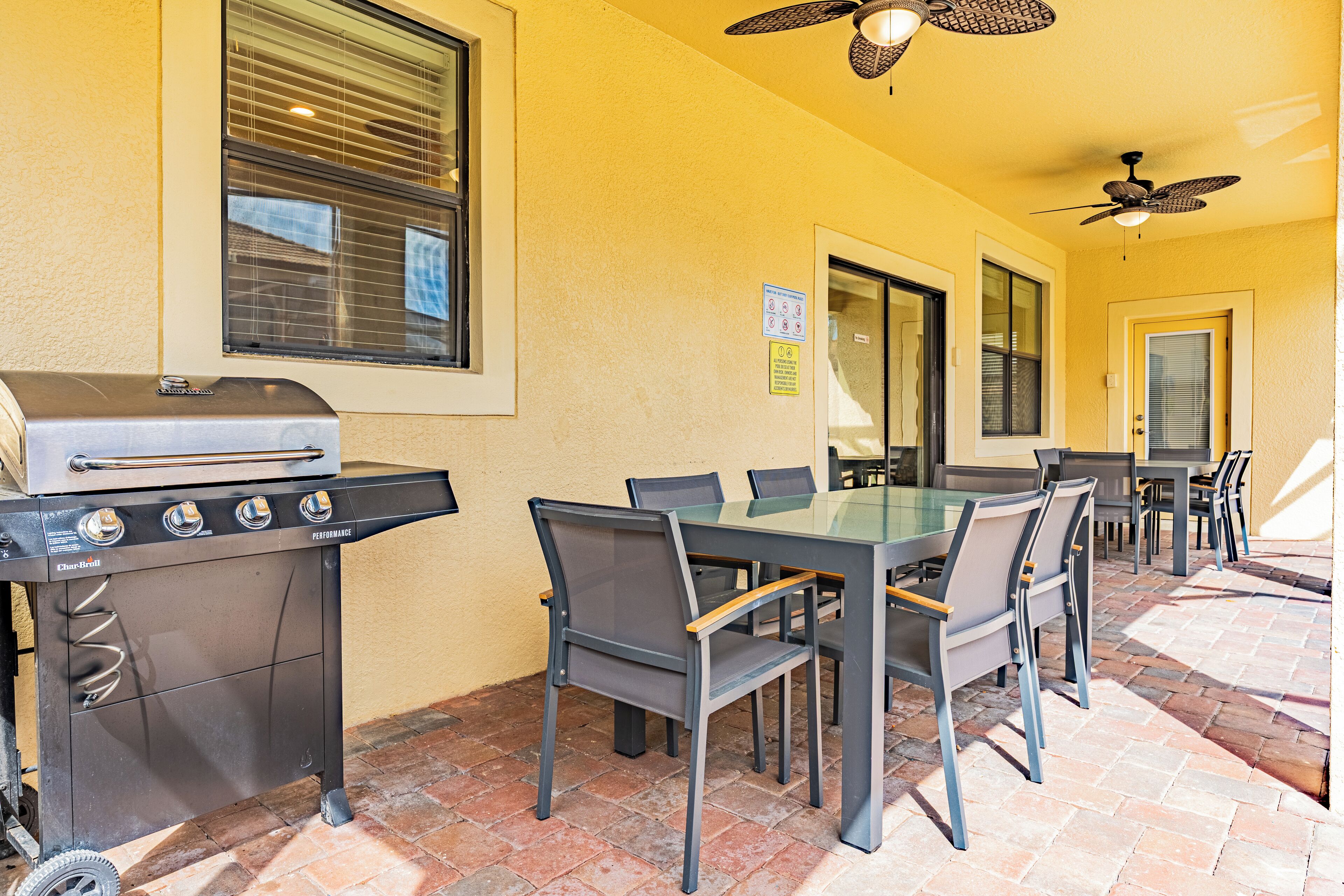 Eine Terrassengruppe mit Grill, Esstisch, Stühlen und Deckenventilatoren.