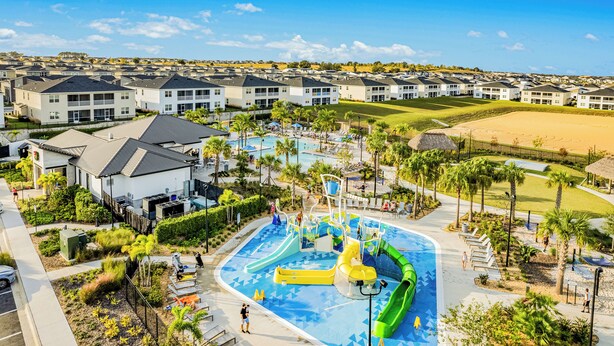 A residential area with a swimming pool and water slides, surrounded by houses and palm trees.