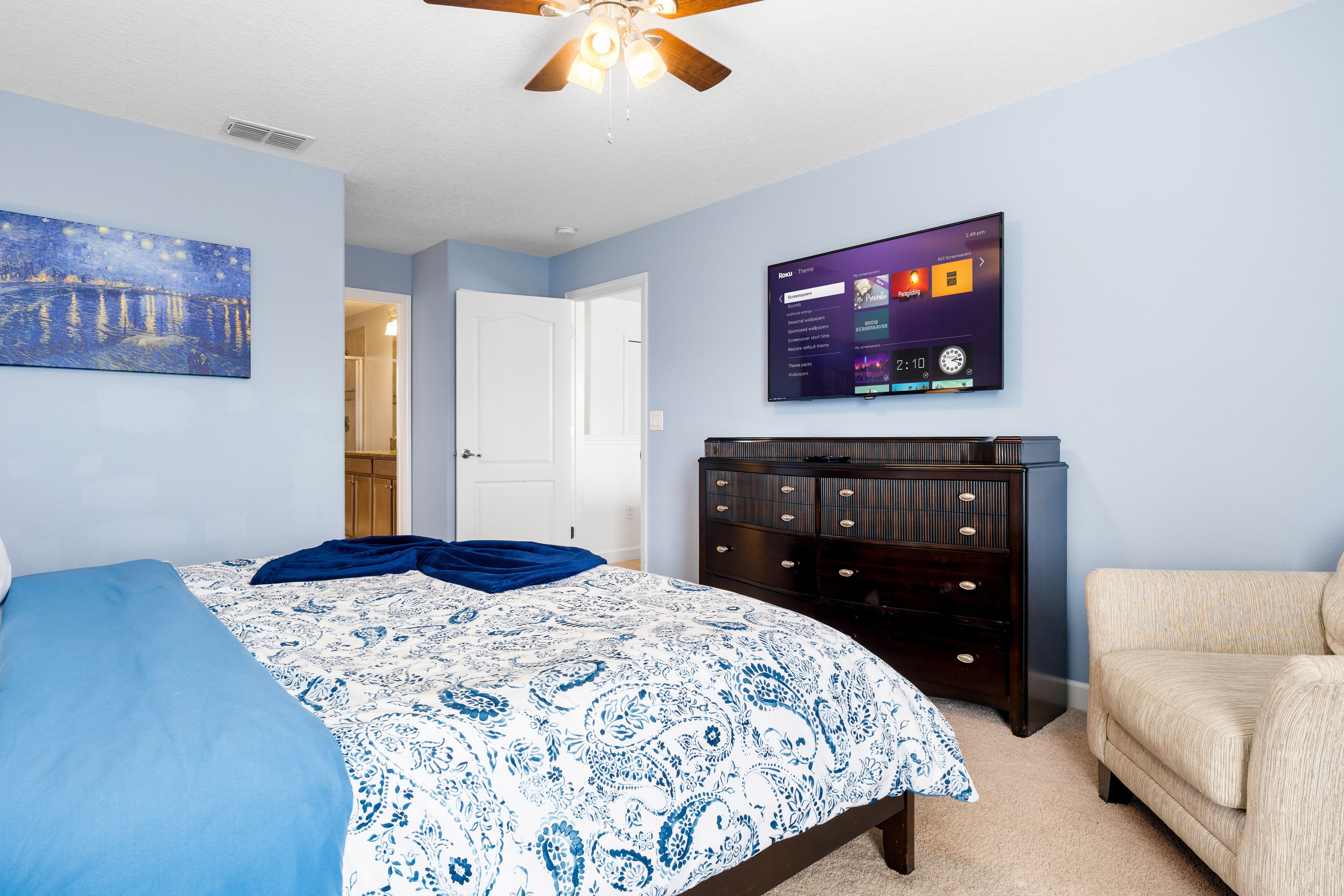 A bedroom with a bed, a dresser, a television, and a ceiling fan.