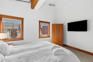 A bedroom with a bed, a TV mounted on the wall, and two windows. - As the sun sets over Leavenworth, the gas fireplace at Klonaqua casts a warm glo (Leavenworth)