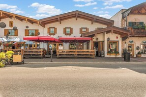 Un bâtiment à la façade traditionnelle, avec des tables à l’extérieur protégées par des parasols rouges, et une enseigne indiquant qu’il s’agit d’un restaurant.