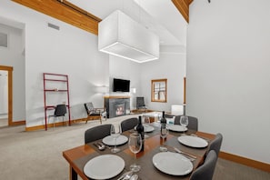 A modern dining area with a wooden table set for four, a fireplace, and a television on the wall. - As the sun sets over Leavenworth, the gas fireplace at Klonaqua casts a warm glo (Leavenworth)