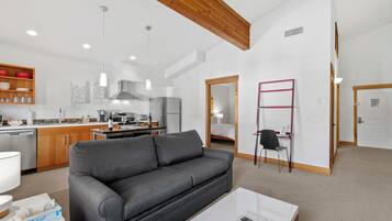 A modern living space with a grey sofa, a white coffee table, and a kitchen area with wooden cabinets and stainless steel appliances.