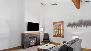 A modern living room with a fireplace, a flat-screen TV, a comfortable sofa, and a window with a view of buildings. - Walk to Village-Fireplace-Festhalle Section (Leavenworth)